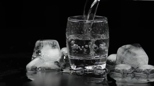 Water is Poured into a Glass with Ice Cubes