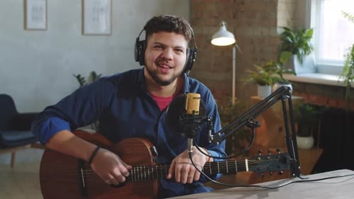 Joyous Musician with Guitar Speaking on Camera in Recording Studio