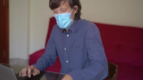 A Young Man Wearing a Face Mask Works From Home During Coronavirus Self-isolation