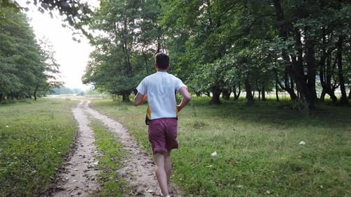 Young Caucasian male running in forest on a trail in summer. Man jogging cross country running on tr