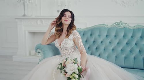 Incredible young woman in a beautiful white wedding dress is sitting on the couch.