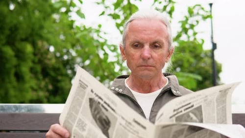 Portrait of Old Man Reading Newspaper on Bench Alone in Park