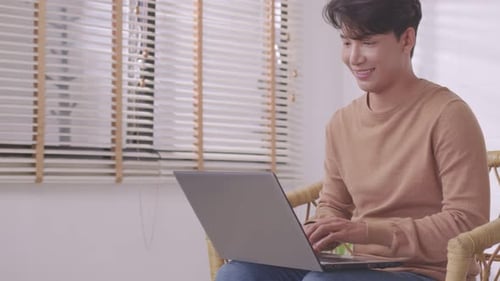 At home, a business asian man types and works online on a desk table with a laptop.