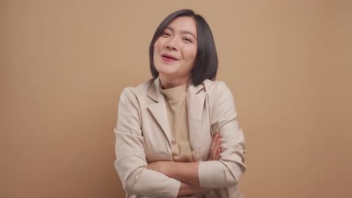 Feliz mujer de negocios asiática de pie y riendo de pie aislada sobre fondo beige. Vídeo 4K