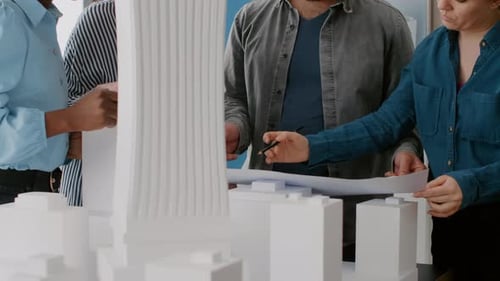 Close Up of Workmates Analyzing Blueprints Plan and Building Model on Table