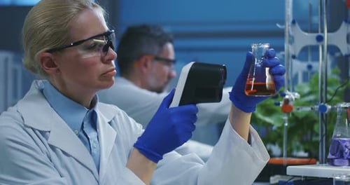 Woman Scientist Inspecting Beaker with Liquid in Lab