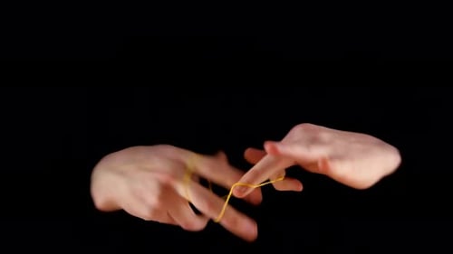 Hands Manipulating a Gold Rubber Band on Black