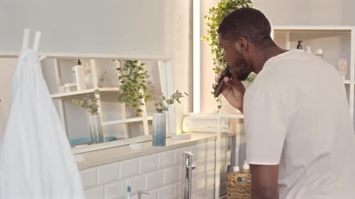 Man Grooming Beard with Electric Trimmer in Bathroom
