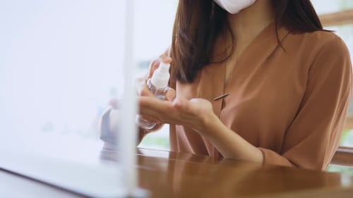 Mulher usando máscara aplicando desinfetante no café