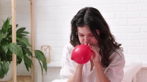 Woman Inflates Red Balloon in Bright Room