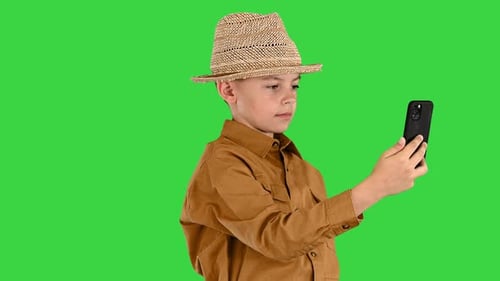Little Boy in a Straw Hat Showing Around While Having Video Call on the Phone on a Green Screen
