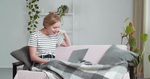 Kaukasische Frau, die zu Hause unter einer Decke auf dem Sofa sitzt, beendet das Gespräch im Video-Chat Online