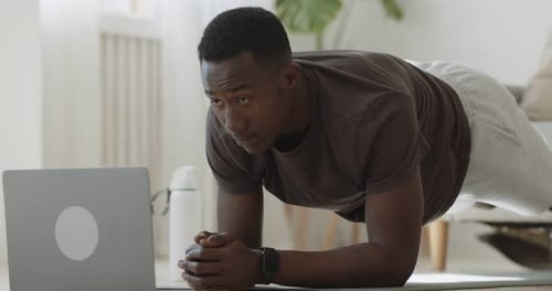 Black Guy Using Standing in Plank Position and Watching Video Tutorial Online on Laptop at Home
