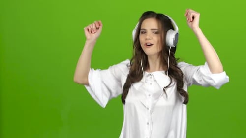 Brunette escucha a través de los auriculares con música enérgica y hace muecas. Pantalla verde