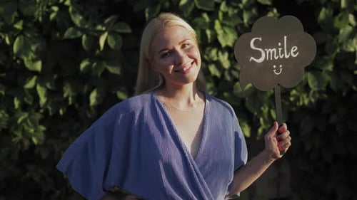 Una hermosa jovencita sonríe y sostiene un cartel que dice «Sonríe». Llame para tener buen humor. Sonríe