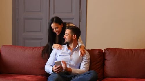 Smiling Couple Looking at Mobile Phone on Couch
