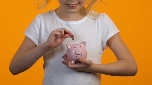 Weibliches Kind legt Münzen ins Sparschwein, Ersparnisse und persönliches Budget, Finanzen