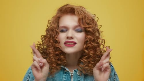 Woman Crossing Fingers on Hands. Worried Girl Praying on Yellow Background