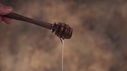 Golden Honey Dripping from Wooden Dipper Close Up
