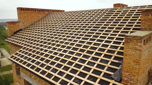 Aerial view of unfinished brick apartment building with wooden roof structure under construction.