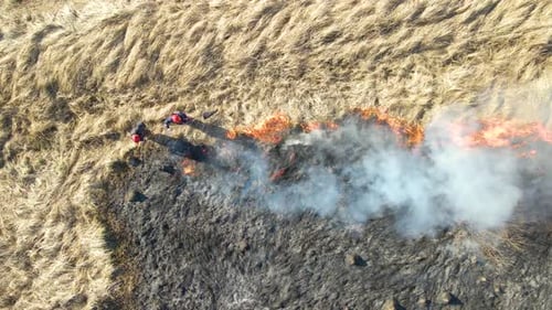 Aerial View of Firemen Extinguishing Grassland Field Burning with Red Fire During Dry Season