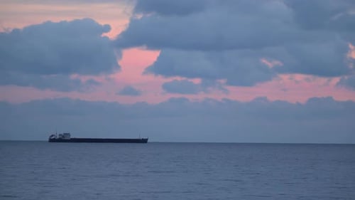 Cargo Ship at Sea Under Colorful Sunrise Clouds