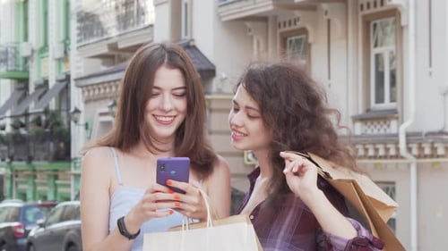 Two Young Women Looking at Phone with Shopping Bags
