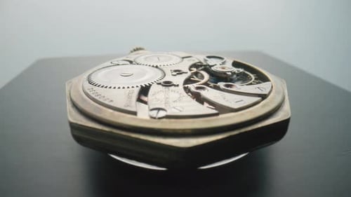 Eine antike Taschenuhr mit einem offenen Uhrwerk dreht sich auf einem grauen Tisch in einem Studio