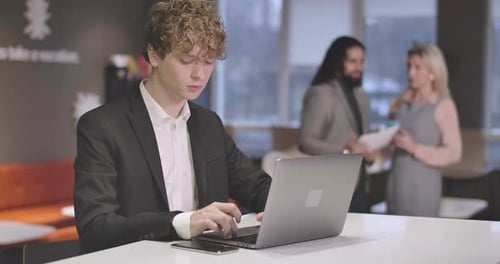 Porträt eines jungen kaukasischen Mannes mit lockigem Haar, der auf einer Laptoptastatur tippt. Porträt von Confident