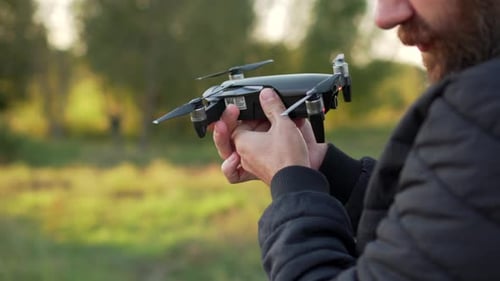 Man Holding and Inspecting Black Drone Outdoors