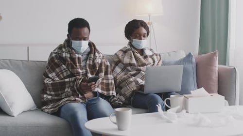 Adults in Blankets Using Tech at Home