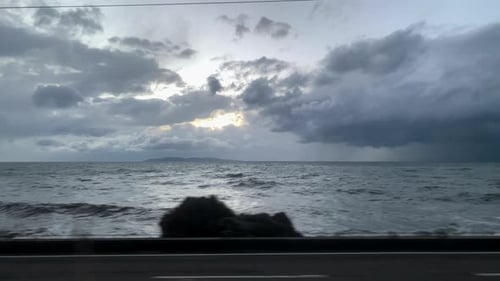 The waves crash against rocks and sun peeks through the clouds. Background sea, sky and sunset. High