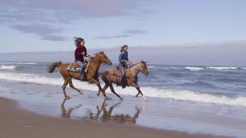 Women riding horses at beach in slow motion