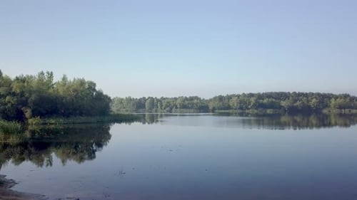 Camera Is Flying Over Small Beach Between Trees in Sunny Calm Weather in Morning