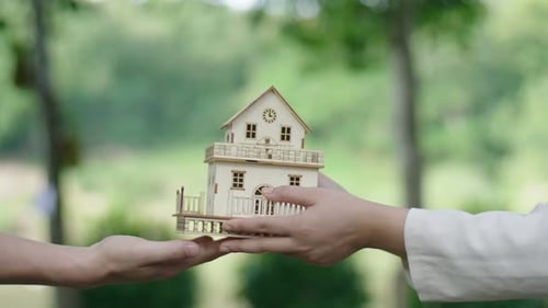 Hands Passing Model House in Green Setting