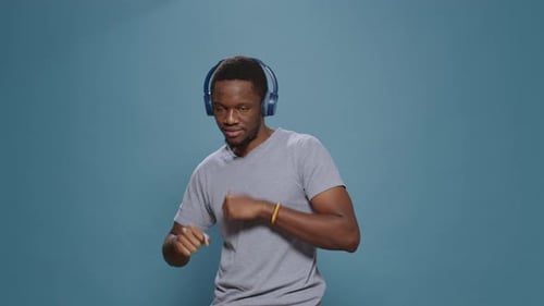 Young Man Dancing with Headphones Against Blue Backdrop