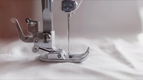 Der silberne Nähfuß der Nähmaschine drückt den Stoff und stickt ihn mit einer Nadel zusammen.
Die