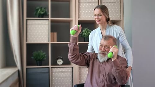 Happy Woman Medical Worker Assistant Training Dumbbells to Disabled Grandfather at Hospital