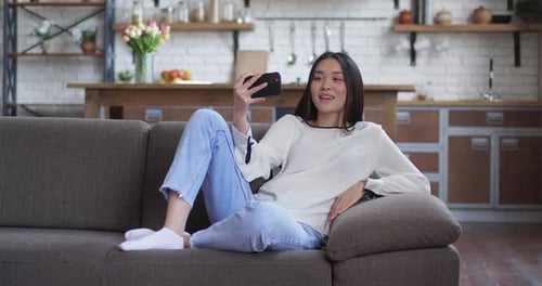 Woman Relaxing on Sofa Using Smartphone for Video Call