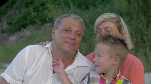 Grandson Tickling Grandfather's Neck While Sitting on Beach