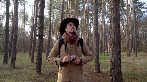Backpacker with Camera Walks Along a Trail in the Forest