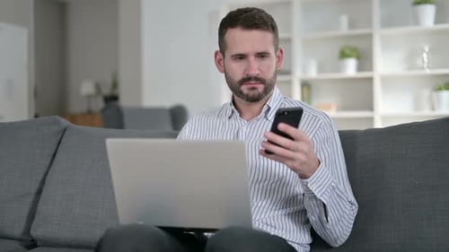 Man Working From Home Using Laptop and Phone