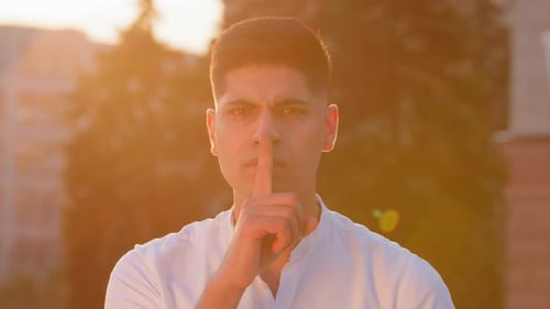 Joven empresario oriental que sostiene el dedo en los labios, mira a la cámara hace que el silencio comparta gestos ocultos