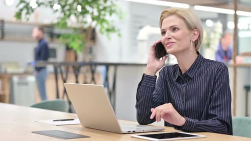 Young Businesswoman with Laptop Talking on Smartphone in Office