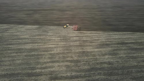 Aerial view of a modern yellow tractor plowing dry agricultural field , preparing land for sowing