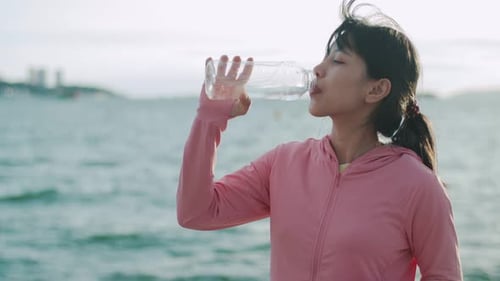 Female runner drinking water while standing on the beach.