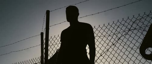 Silhouette of Person Standing by Barbed Wire Fence