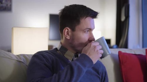 Man Drinking From Mug, Relaxing on Couch at Home