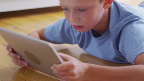 Boy Lies On Floor Using Tablet Indoors