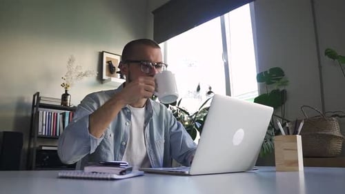 Man Typing on Laptop and Drinking from Mug